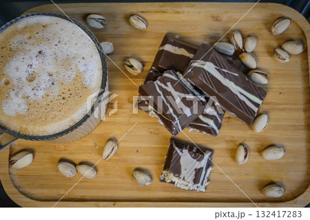 Overhead shot of a coffee cup with foamy coffee accompanied by chocolate pieces topped with nuts. Perfect for food photography, cozy breakfast, desserts, coffee breaks, and lifestyle concepts. 132417283