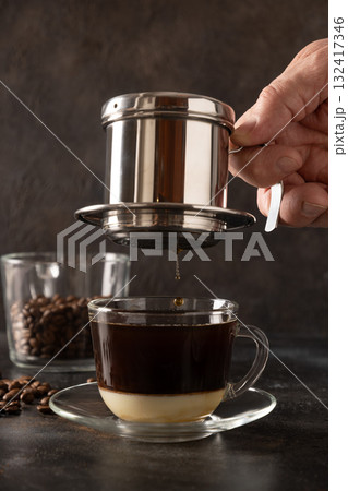 Brew Vietnamese coffee with sweet condensed milk in glass cup by traditional method on black background. Close up. Brew Vietnamese coffee with sweet condensed milk in glass cup by traditional method on black background. Close up. 132417346