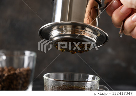 Brew Vietnamese coffee with sweet condensed milk in glass cup by traditional method on black background. Close up. Brew Vietnamese coffee with sweet condensed milk in glass cup by traditional method on black background. Close up. 132417347