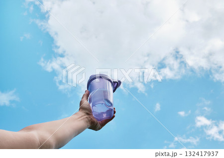 Female hand holding bottle of water against blue sky Female hand holding bottle of water against blue sky 132417937