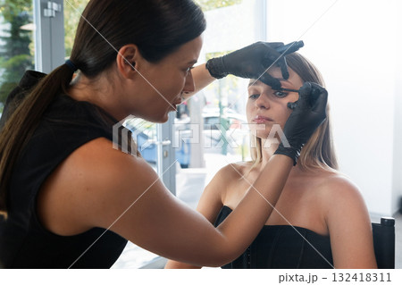 Professional makeup artist applying eyeliner to a model in a bright studio during a beauty session 132418311
