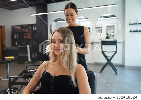 Professional hairstylist creates a beautiful look for a smiling client in a modern salon during the daytime Professional hairstylist creates a beautiful look for a smiling client in a modern salon during the daytime 132418324