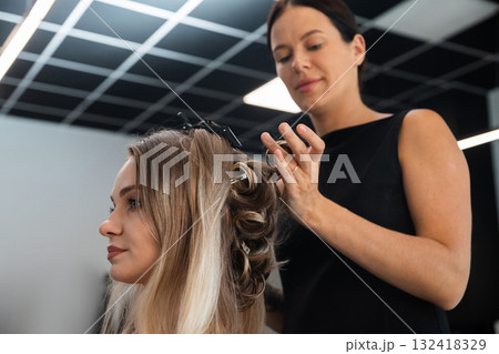 Hair stylist creates elegant curls for client in modern salon setting on a bright afternoon, showcasing expert techniques and stylish design Hair stylist creates elegant curls for client in modern salon setting on a bright afternoon, showcasing expert techniques and stylish design 132418329