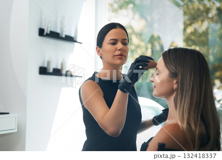 Makeup artist applying foundation to a client's face in a bright, modern beauty studio during the day Makeup artist applying foundation to a client's face in a bright, modern beauty studio during the day 132418337
