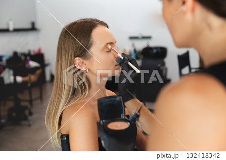 Makeup artist applies foundation on client in well-lit salon during daytime Makeup artist applies foundation on client in well-lit salon during daytime 132418342