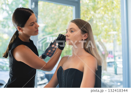 Makeup artist applies cosmetics to a model during a beauty session at a bright studio in the afternoon Makeup artist applies cosmetics to a model during a beauty session at a bright studio in the afternoon 132418344