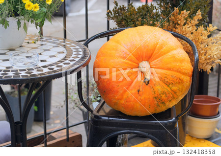 Large orange pumpkin on chair near a street table. Pumpkin in autumn decor of street cafe. 132418358