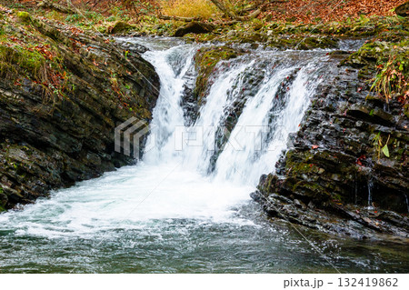 autumn scenery with waterfall. stones seen through transparent water. orange foliage on the hill. cascades of the river turychka in fall season. overcast weather. travel destination of transcarpathia autumn scenery with waterfall. stones seen through transparent water. orange foliage on the hill. cascades of the river turychka in fall season. overcast weather. travel destination of transcarpathia 132419862