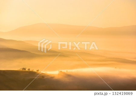 abstract landscape of carpathian mountains in autumn fog at sunrise. beautiful view over the perechyn valley. rolling hills of ukraine in sea of golden light and mist. atmospheric phenomenon photo 132419869