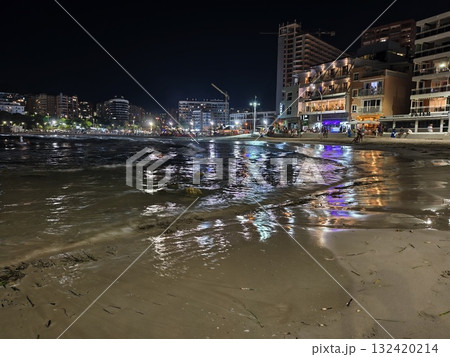 nighttime reflections on urban seascape, calm harbor scene with shimmering city lights and wet sand nighttime reflections on urban seascape, calm harbor scene with shimmering city lights and wet sand 132420214