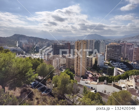 sunlit rooftops and distant horizon, urban hillside overlooking city skyline with mountain backdrop 132420346