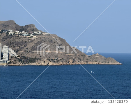 picturesque hillside village on sunlit coastline overlooking serene blue sea and rocky shore 132420370