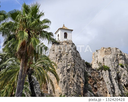 enchanting image of white bell tower atop rocky outcrop surrounded by palm trees and cloudy sky enchanting image of white bell tower atop rocky outcrop surrounded by palm trees and cloudy sky 132420428