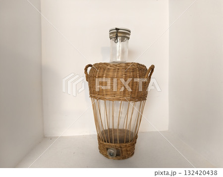 woven basket holding aged glass demijohn, vintage wicker demijohn bottle in rustic setting 132420438
