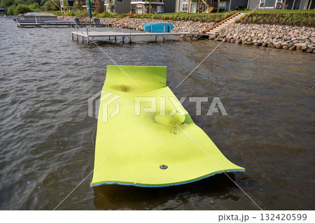 Kids having fun on a floating mat in the lake during a sunny summer day near cozy lakeside houses Kids having fun on a floating mat in the lake during a sunny summer day near cozy lakeside houses 132420599