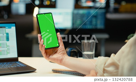 Office worker holding her smartphone with chroma key screen at desk, solving tasks after hours alone in the corporate workspace. Woman employee engaged in enterprise management. Camera B. Office worker holding her smartphone with chroma key screen at desk, solving tasks after hours alone in the corporate workspace. Woman employee engaged in enterprise management. Camera B. 132420788