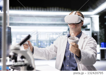 Researcher in lab workspace uses VR headset to explore three dimensional models of cellular biology. The simulation highlights innovation in biotechnology research and molecular science. Researcher in lab workspace uses VR headset to explore three dimensional models of cellular biology. The simulation highlights innovation in biotechnology research and molecular science. 132420795