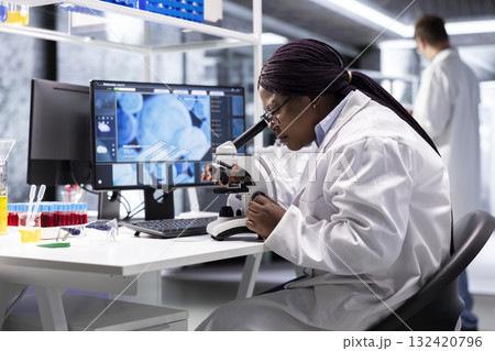 Black scientist examining samples under microscope in a modern laboratory. Research work integrates biotechnology, molecular science and advanced diagnostics to shape medical discovery. Black scientist examining samples under microscope in a modern laboratory. Research work integrates biotechnology, molecular science and advanced diagnostics to shape medical discovery. 132420796