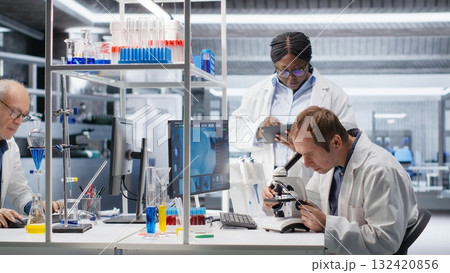 Team of experts investigate molecular samples at microscope with laboratory tray and lens system, magnification tools support diagnostics and biotechnology breakthrough in science. Team of experts investigate molecular samples at microscope with laboratory tray and lens system, magnification tools support diagnostics and biotechnology breakthrough in science. 132420856