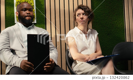 Black male job seeker waiting to be called after a person in front of him, sitting in queue on the hallway with his registration files and CV in hand. Calling in candidates. 132420862