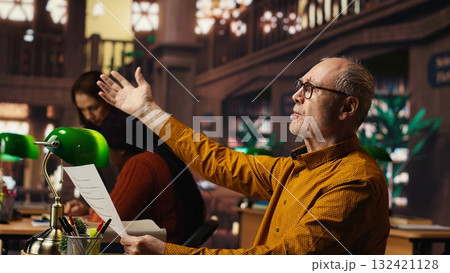 Elderly actor in a library focusing on script reading and memorization, preparing for a classic drama play with dedication and passion for theatre performance. Dramatic arts. 132421128