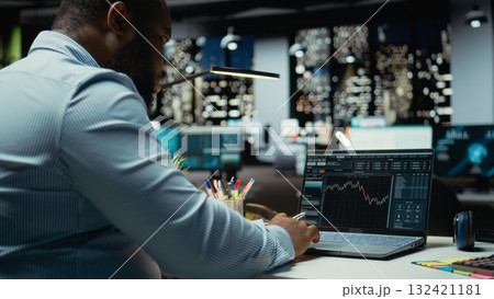 African american consultant examining data on stock and forex trading, preparing reports and forecasts that drive business development. Building a modern investment strategy at night. 132421181