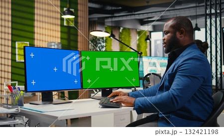 African american businessman examines reports with isolated dual monitors, building a new business strategy for global development. Objectives alignment with productivity. African american businessman examines reports with isolated dual monitors, building a new business strategy for global development. Objectives alignment with productivity. 132421198