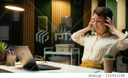 Employee working on tasks with focus music and stretching her muscles, using headset to help with concentration and productivity. Woman multitasking and correcting her posture. Camera B. Employee working on tasks with focus music and stretching her muscles, using headset to help with concentration and productivity. Woman multitasking and correcting her posture. Camera B. 132421199