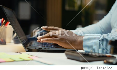 Close up of black worker proofreading and fact checking financial data, reviewing archived files after hours in strategy room. Evaluating reports, researching and organizing agenda. 132421221