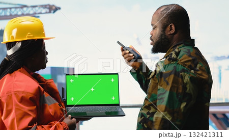 Chroma key laptop used by soldier on offshore platform communicating via military radio. Naval unit on drilling barge using green screen mockup notebook, speaking on walkie talkie 132421311