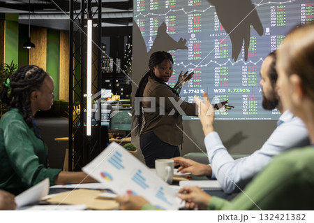 Team leader presenting data forecasting trends on projection board, shares infographics data with colleagues in a night time meeting. Corporate event to plan project development. 132421382