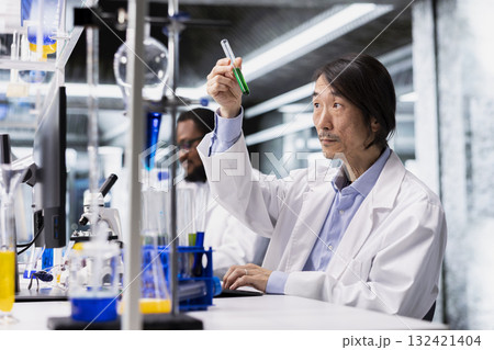 Senior laboratory chemist inspects clarity of chemical solution in vial for purity verification. Biochemist at work prepares reagent vials for assay procedures during clinical trials 132421404