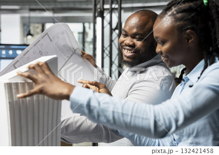 Diverse architectural team reviews 3D models and blueprints for a construction site, respecting zoning regulations and other details. Teamwork for site preparation, urban development. 132421458