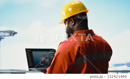 Fossil fuel company expert using laptop software to determine optimal drilling rig locations. African american man on offshore platform looking at well sites data on notebook Fossil fuel company expert using laptop software to determine optimal drilling rig locations. African american man on offshore platform looking at well sites data on notebook 132421460