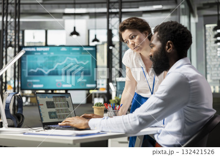 Female team leader and male staff discussing innovative strategies, evaluating data and insights in laptop. Diverse colleagues in office, working as team to improve outcomes and foster company growth. 132421526