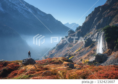 Woman standing on rock near a waterfall in Swiss Alps in autumn Woman standing on rock near a waterfall in Swiss Alps in autumn 132421607