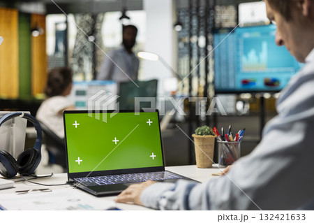 Business consultant seated at desk, looking at laptop with green screen display. Caucasian male professional focused on financial planning using digital device showing blank chroma key template. 132421633