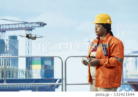 Drilling barge engineer using drone to access areas that pose safety risks to humans from safe distance. Woman on offshore platform deck uses remote control UAV to conduct aerial inspection Drilling barge engineer using drone to access areas that pose safety risks to humans from safe distance. Woman on offshore platform deck uses remote control UAV to conduct aerial inspection 132421644