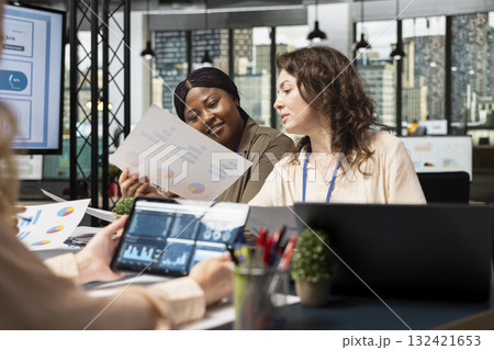 Group of business associates meeting in boardroom to align performance goals with project indicators, surrounded by reports and digital tools. Ambitious team showcasing collective success. Group of business associates meeting in boardroom to align performance goals with project indicators, surrounded by reports and digital tools. Ambitious team showcasing collective success. 132421653