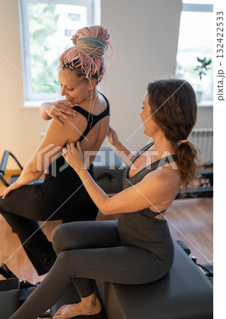 Pilates instructor adjusts posture, instructor meticulously corrects shoulder posture during session Pilates instructor adjusts posture, instructor meticulously corrects shoulder posture during session 132422533