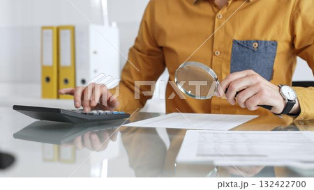 Accountant analyzing financial data with magnifying glass, calculating expenses, and auditing documents at office desk. Audit and taxes in business Accountant analyzing financial data with magnifying glass, calculating expenses, and auditing documents at office desk. Audit and taxes in business 132422700
