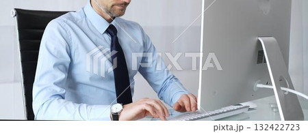 Mature businessman in office concentrating on important computer work, typing on keyboard, engaging in professional tasks, representing technology, development, and progress 132422723