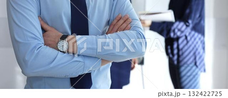 Confident businessman standing with arms crossed at a corporate meeting, leading a team of professionals discussing business strategies and plans in an office workspace 132422725