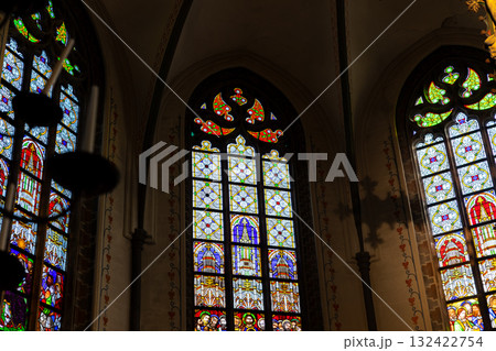 Intricate stained glass windows illuminate a historic church interior with vibrant color and sacred detail. Gothic arches symbolic imagery create a serene and spiritual atmosphere filled with light Intricate stained glass windows illuminate a historic church interior with vibrant color and sacred detail. Gothic arches symbolic imagery create a serene and spiritual atmosphere filled with light 132422754