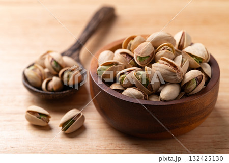 Roasted Pistachio nuts in a bowl with spoon on wooden background Roasted Pistachio nuts in a bowl with spoon on wooden background 132425130