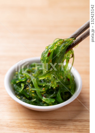 Wakame seaweed salad with sesame seed in a bowl with chopsticks on wooden background 132425142