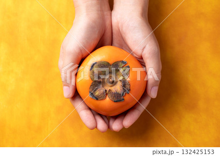 Ripe persimmon fruit holding by hand on orange color background, Autumn fruit, Top view Ripe persimmon fruit holding by hand on orange color background, Autumn fruit, Top view 132425153