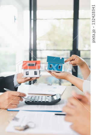 Close up of real estate agent showing small house model to client with calculator, contract paperwork on desk, concept of mortgage loan, home ownership, property investment agreement. mortgage loan 132428341
