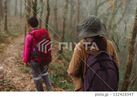 Two hikers walking together on forest trail in foggy weather with backpacks and trekking poles, symbol of adventure, teamwork, outdoor lifestyle, exploration, journey and travel inspiration. 132428347