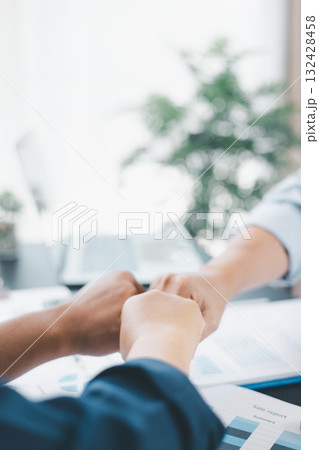 Business teamwork concept with three colleagues doing fist bump in office, symbol of partnership, trust, support and successful collaboration with financial reports on desk. 132428458
